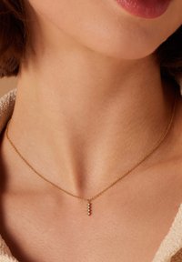 Gouden ketting met een kleine, verticale hanger waarop vier sprankelende kristallen staan. Zachte textuur tegen de huid, elegant ontwerp.