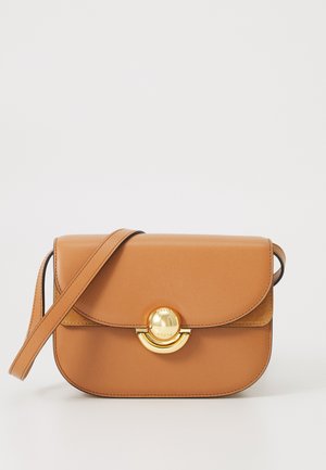 Ruda odinė kryžminė rankinė su apvalia forma, auksinės spalvos užsegimas ir plona petneša. Lygus paviršius, minimalizmo stilius.