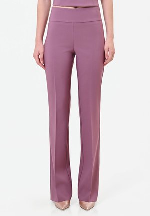 Donna che indossa pantaloni malva a vita alta e gamba dritta abbinati a un top coordinato e décolleté beige con punta appuntita su sfondo bianco.