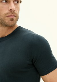 Dark green, short-sleeve t-shirt made of ribbed fabric. Features a round neckline and fitted design with minimal stitching details.