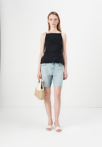 Zwarte mouwloze top met een geplooide textuur, lichtblauwe denim shorts, crèmekleurige slide sandalen en een beige geweven tas. Eenvoudig en modern ontwerp.