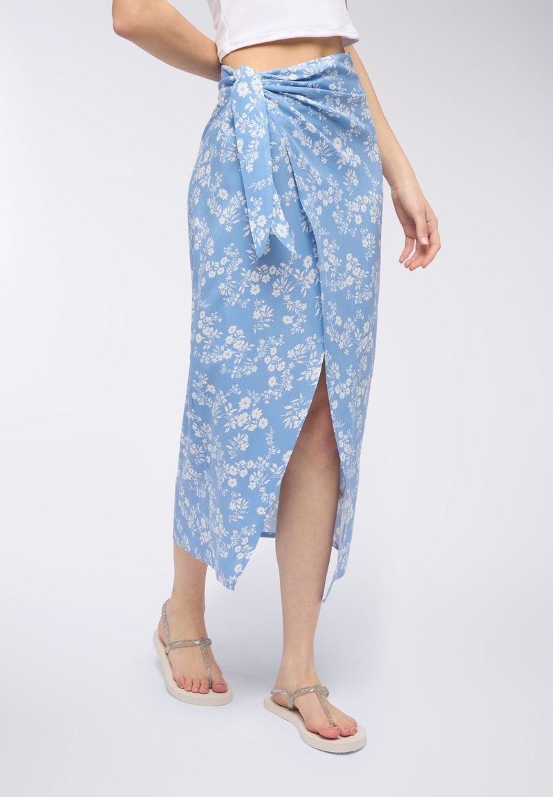 Gonna a portafoglio blu a fiori realizzata in tessuto leggero, con uno spacco laterale e vita annodata. Abbinata a semplici infradito.