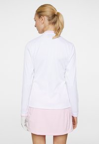 Vit långärmad topp med ribbat mönster och rosa detaljer vid kragen och ärmsluten, kombinerad med en ljusrosa kjol.