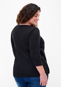 Black long-sleeve shirt with a round neckline. Soft fabric, relaxed fit, and slightly curved hem. Worn with blue jeans, showing a casual look.