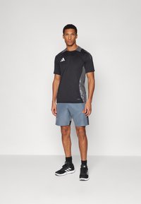 Svart idretts-T-skjorte med grå detaljer og tre-stripes logo, kombinert med grå shorts med oransje detaljer og svarte joggesko.