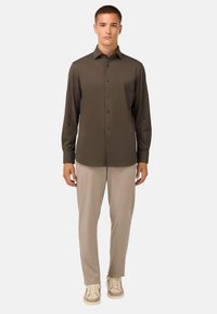 Tumši olīvzaļš garām piedurknēm krekls ar pogu aizdari, apvienots ar gaiši beicētiem biksēm un beicētām sporta apaviem. Gluda auduma, pielāgota silueta.