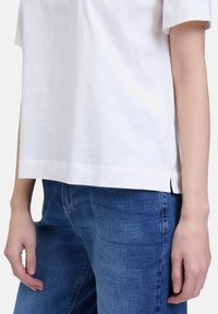 White cotton T-shirt with a loose fit, short sleeves, and side slits, paired with blue denim jeans featuring a classic blue wash.