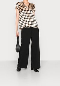 Svart och gräddfärgad kortärmad topp med ett geometriskt mönster, tillsammans med lösa svarta byxor och en liten svart handväska.