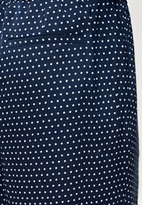 Υφασμα σκούρου μπλε με λευκές πουά, που διαθέτει οριζόντια σχισμή-τσέπη σε ένδυμα.