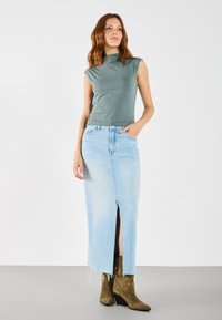 Grønn ermeløs topp kombinert med et lyseblått denim maxiskjørt med en frontslitting, komplementert av brune suedestøvletter.
