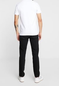 Vaqueros de mezclilla negra con un corte recto, combinados con una camiseta blanca básica. Zapatillas blancas completan el atuendo. Tatuaje visible en el brazo.