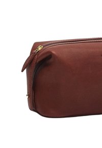 Brown leather cosmetic bag with a textured surface, zip closure, and gold-tone zipper hardware. Rounded shape with a flat base.