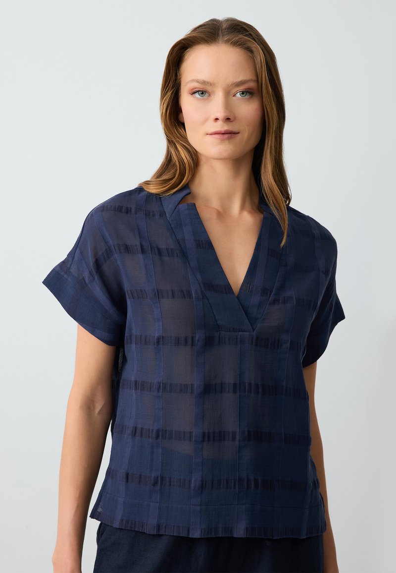 Marineblaues kurzärmliges Blusenshirt mit V-Ausschnitt, aus transparentem Stoff mit horizontalen und vertikalen Strukturstreifen. Glatte Oberfläche.