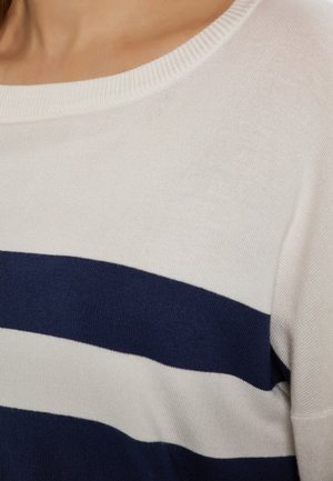 Pletený svetr s širokým bílým tělem a modrými horizontálními pruhy. Výstřih do lodičky a jemná textura.