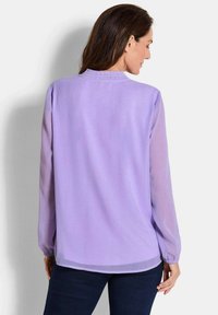 Blusa a maniche lunghe lavanda con collo arricciato e maniche trasparenti. Presenta una vestibilità ampia e un orlo leggermente curvato, realizzata in tessuto leggero.