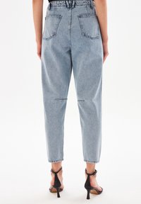 Světlé modré džíny z denimu s vysokým pasem, zúženými nohavicemi a dvěma zadními kapsami. Materiál má měkkou texturu s minimálním opotřebením.