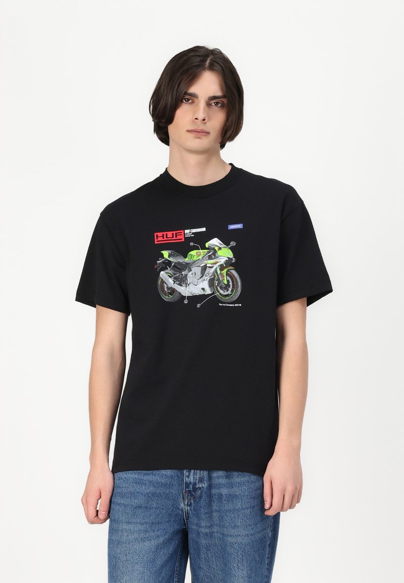 Zwart katoenen t-shirt met een grafisch ontwerp van een motorfiets in groen en zilver, met tekst en logo's in rood en blauw. Korte mouwen, ronde hals.