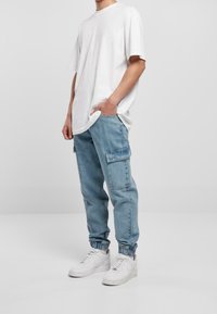 Bílý oversized tričko, modré džínové cargo kalhoty s bočními kapsami a bílé tenisky s kulatou špičkou a šněrováním.