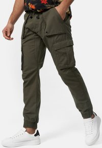 Pantalons cargo en vert olive, avec plusieurs poches, des poignets élastiques et une coupe décontractée. Assortis à des baskets blanches pour un contraste.
