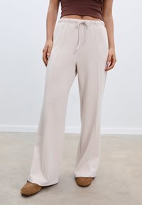 Helle beige, weite Hosen mit elastischem Bund und Kordelzug. Glatte Textur mit Seitennähten; kombiniert mit braunen Schuhen.