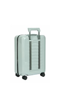 Valise à coque dure vert clair de taille cabine avec quatre roues pivotantes noires et une poignée rétractable dépliée.