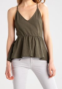 Top peplum verde oliva con spalline sottili, scollatura a V e vestibilità ampia. Realizzato in tessuto morbido con una texture fluida.
