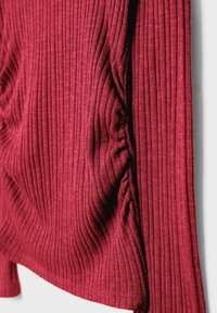 Roter gerippter Stoff mit strukturiertem Detail und gerafftem Abschnitt. Weiches Material mit vertikalen Linien, das eine subtile Tiefe und Bewegung erzeugt.