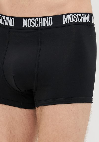 Čierne boxerky vyrobené z mäkkej tkaniny, so čiernym elastickým pásom s bielym značkovaním "MOSCHINO". Hladký povrch, priliehavý strih.
