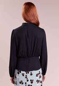 Svart blus med långa ärmar, figursydd midja och dragkedja i ryggen. Slät textur med rynkdetaljer vid midjan. Mönstrad flerfärgad kjol nedan.