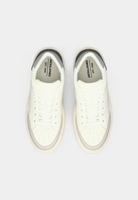 Une paire de baskets Jack & Jones blanc cassé avec des lacets, une zone de orteil perforée et des accents gris, vues de dessus sur un fond blanc.