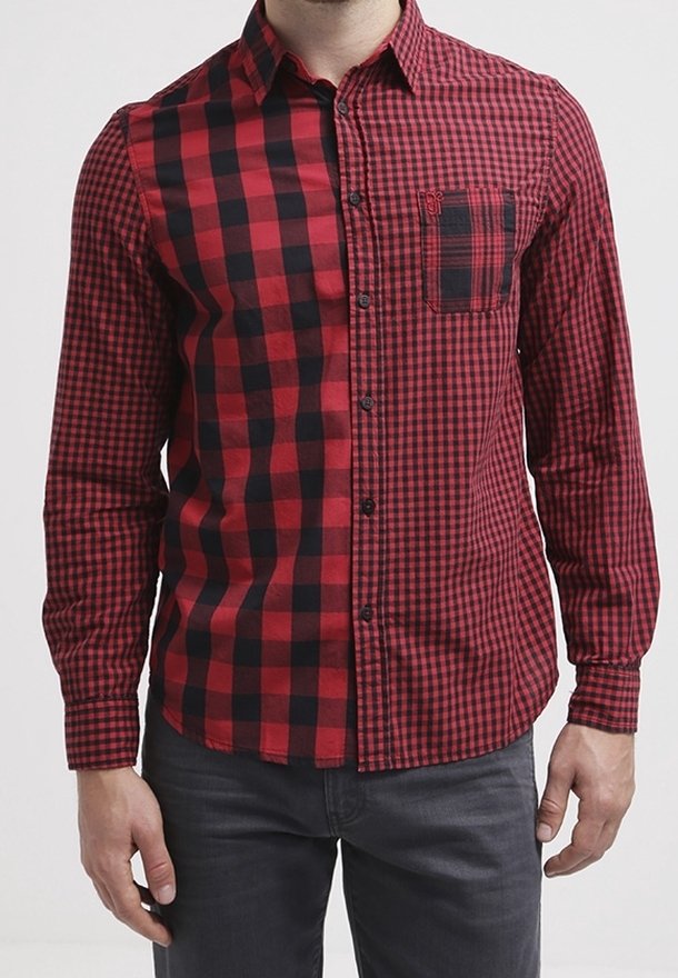 Homme portant une chemise à carreaux rouge et noire avec deux motifs de carreaux différents et une petite poche poitrine sur le côté gauche.