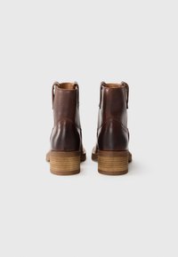 Braune Leder-Ankle-Boots mit glatter Oberfläche und strukturiertem Rücken, ausgestattet mit einem gestapelten Holzabsatz und Zuglaschen für ein einfaches An- und Ausziehen.