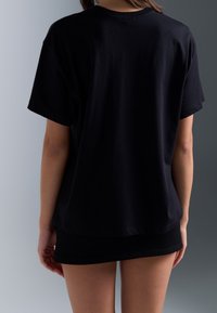 Mustavi puuvillane T-särk lühikeste varrukatega, lahtine lõige ja ümmargune kaelus, vaadatakse tagantpoolt. Sile tekstuur, nähtavad mustrid või aktsendid puuduvad.