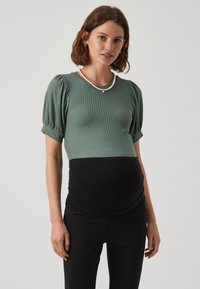 Haut vert côtelé à manches courtes avec manches bouffantes, associé à un pantalon de maternité noir, doté d'une ceinture élastique pour le confort.