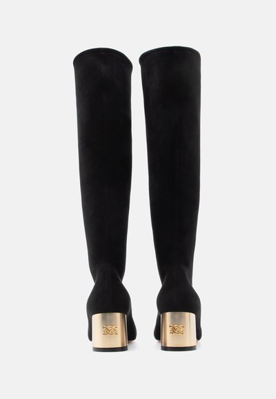 Botas de camurça preta acima do joelho com biqueira arredondada e saltos blocados dourados com detalhe de logótipo em relevo. Textura suave e design elegante.