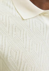 Polo tričko v jasně krémové barvě z bavlněného pleteného materiálu, s texturovaným geometrickým vzorem, límcem a zapínáním na tři knoflíky.