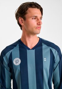 Marinblå och teal-randig sportt-shirt med V-ringning, kort ärm, perforerad struktur och rund logotyp på vänster bröst.