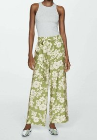 Lichtgrijze mouwloze top gecombineerd met losse, wijde groene broek met bloemenpatroon. Glad materiaal, tailleband met strikdetail en metallic schoenen.