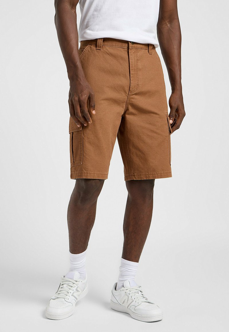 Shorts cargo marrones de corte holgado, con bolsillos laterales y un material de algodón duradero. Combinados con zapatillas blancas y calcetines hasta la mitad de la pantorrilla.