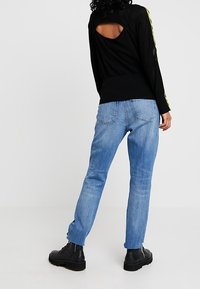 Maglione nero a maniche lunghe in rete con schiena scoperta, abbinato a jeans dritti azzurri chiari e stivaletti neri con lacci alla caviglia.