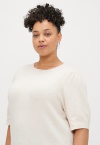 Μπεζ, άνετο πουλόβερ με στρογγυλή λαιμόκοψη και κοντά φουσκωτά μανίκια. Φτιαγμένο από μαλακό υλικό με ελαφριά υφή, κατάλληλο για casual εμφάνιση.