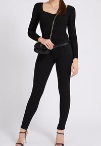 Zwart geribd topje met lange mouwen en een vierkante halslijn, gecombineerd met zwarte skinny jeans, een zwarte tas met ketting en zwarte sandalen met bandjes.