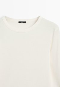 Hvid langærmet t-shirt lavet af blødt bomuld, med en rund halsudskæring og minimale syninger. Etiketten er synlig ved halsen.