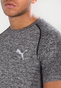 Grå, åtsittande atletisk t-shirt med en strukturerad tyg, korta ärmar och en vit Puma-logotyp på vänster bröst.