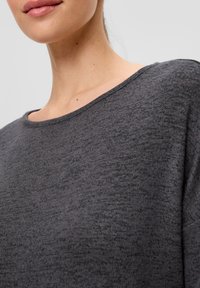 Haut en tricot gris foncé avec un décolleté large et une texture douce, présentant une coupe décontractée qui tombe doucement sur les épaules.