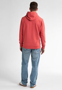 Felpa corallo con cappuccio e cordino, in misto cotone, con polsini e orlo a costine, abbinata a jeans azzurri e sneakers bianche.