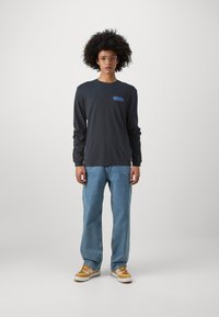 Langærmet mørkegrå bomuldstrøje med rød og blå grafisk design, parret med lysblå lige ben denim jeans og beige sneakers.