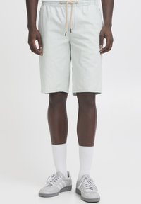 Svetlo zelene kratke hlače z elastičnim pasom, z zategovalnim vrvico in stranskimi žepi. Kombinirane s sivimi supergami in belimi nogavicami.