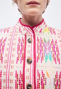 Χρωματιστό κεντητό μπουφάν σε εκρού χρώμα με ροζ λεπτομέρειες, που διαθέτει στενή γιακά μανταρίνι, κουμπώματα με κουμπιά και γεωμετρικά μοτίβα.