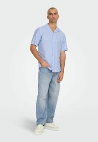 Ljusblå kortärmad skjorta med krage, i kombination med ljusblå jeans och vita sneakers. Slät tygtextur och avslappnad passform.